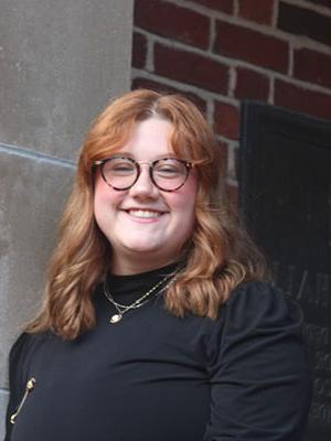 white woman with red hair wearing glasses a black shirt with gold necklaces